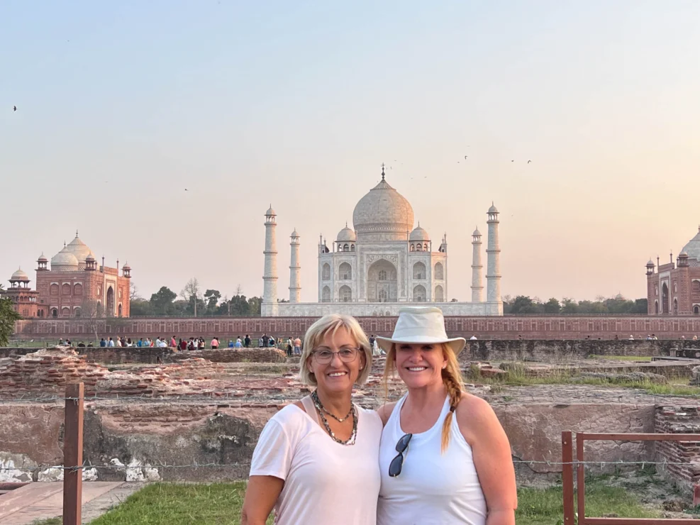 Two women pose in front of the Taj Mahal during daytime.