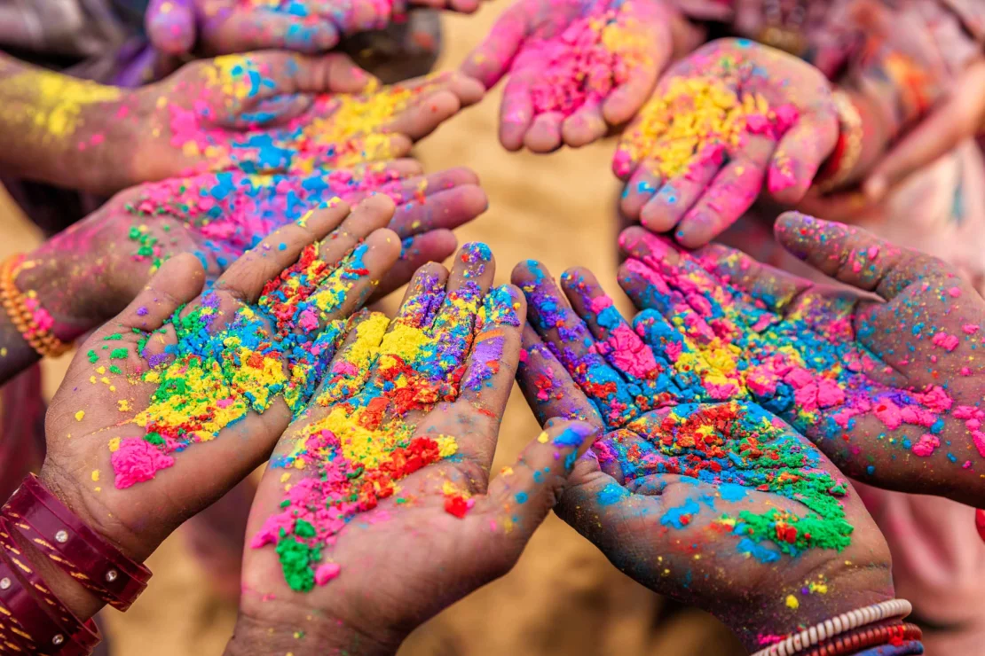 Hands covered in vibrant colored powders reaching into the center, celebrating the festival of Holi.