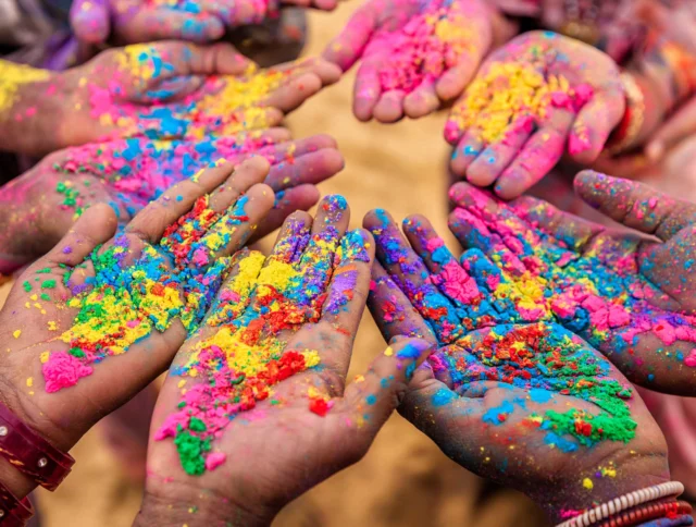 Hands covered in vibrant colored powders reaching into the center, celebrating the festival of Holi.