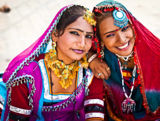 Two women in vibrant traditional attire and jewelry, smiling.