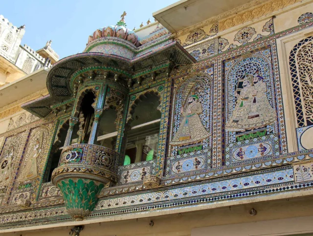 Ornate palace facade with intricate mosaics and decorative balcony, featuring detailed artwork and carvings under a clear sky.