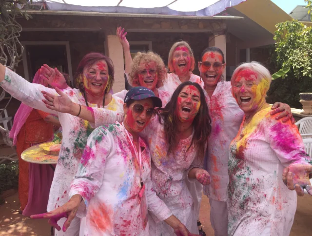 Group of people celebrating Holi, covered in colorful powder, smiling and posing outdoors.