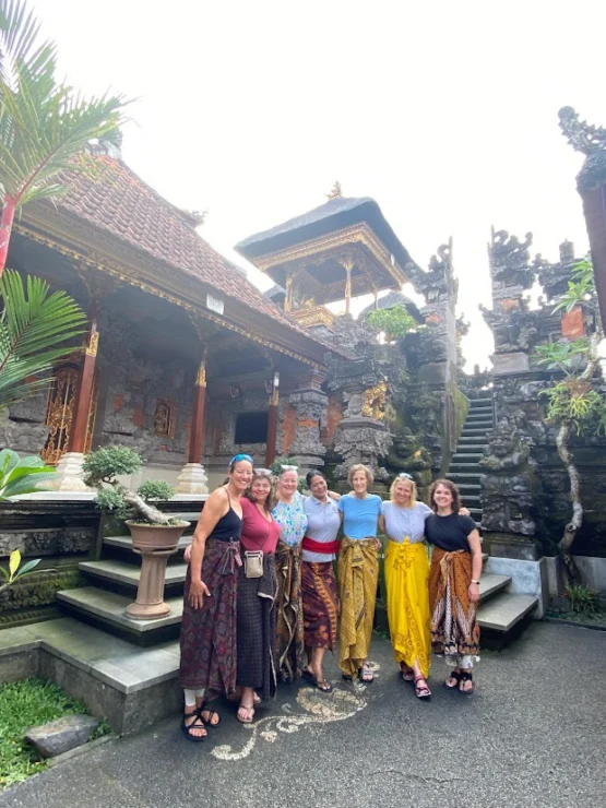 A group of six women stand together in front of traditional Balinese architecture.