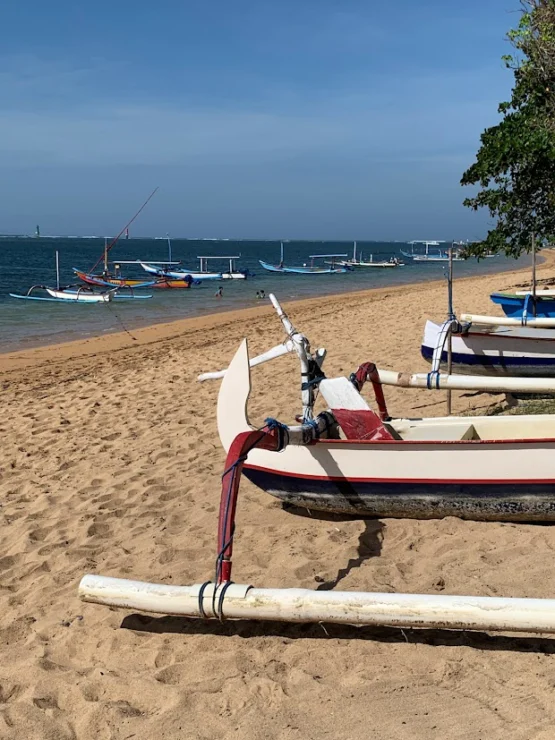 Traditional boats on a sandy beach with a clear blue sky and calm sea in the background.