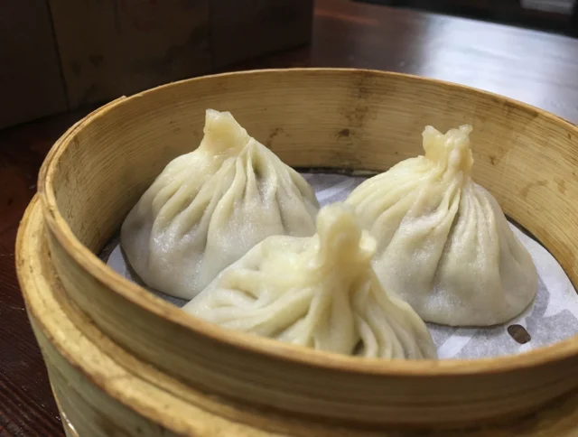 Three steamed dumplings in a bamboo steamer basket on a wooden table.