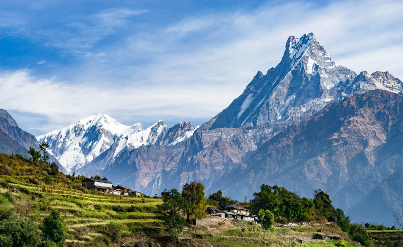 Scenic mountain landscape with snow-capped peaks and lush terraced fields, under a clear blue sky.