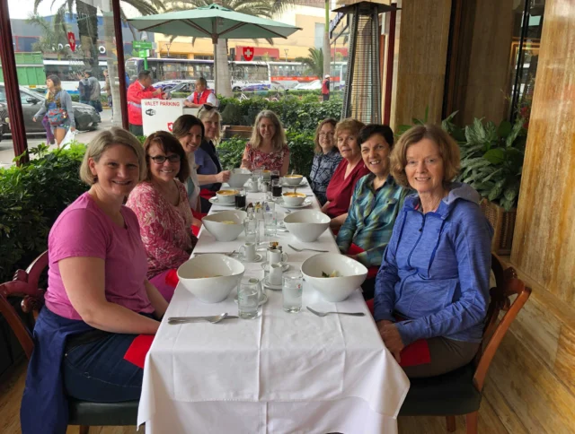 Eight people are seated around a table in a restaurant, smiling at the camera. Plates and glasses are on the table.