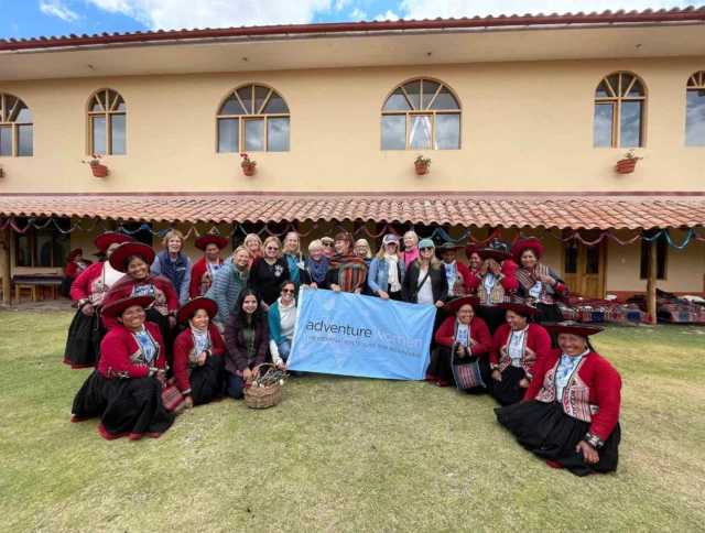 Group of women posing in front of a building, holding a banner that reads "adventure women." Several are wearing colorful traditional attire.