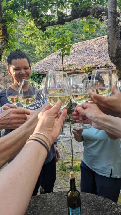 A group of people clink glasses of white wine outdoors near a rustic building.