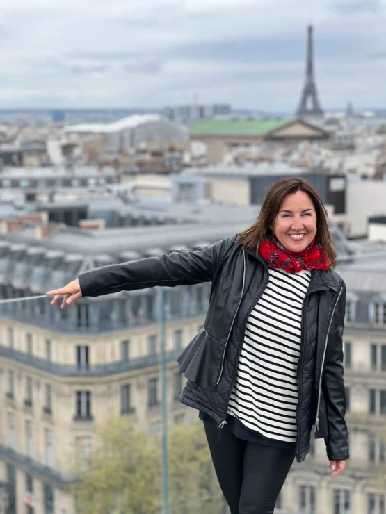 Person smiling with arm outstretched on a rooftop, with the Eiffel Tower and a cityscape in the background.