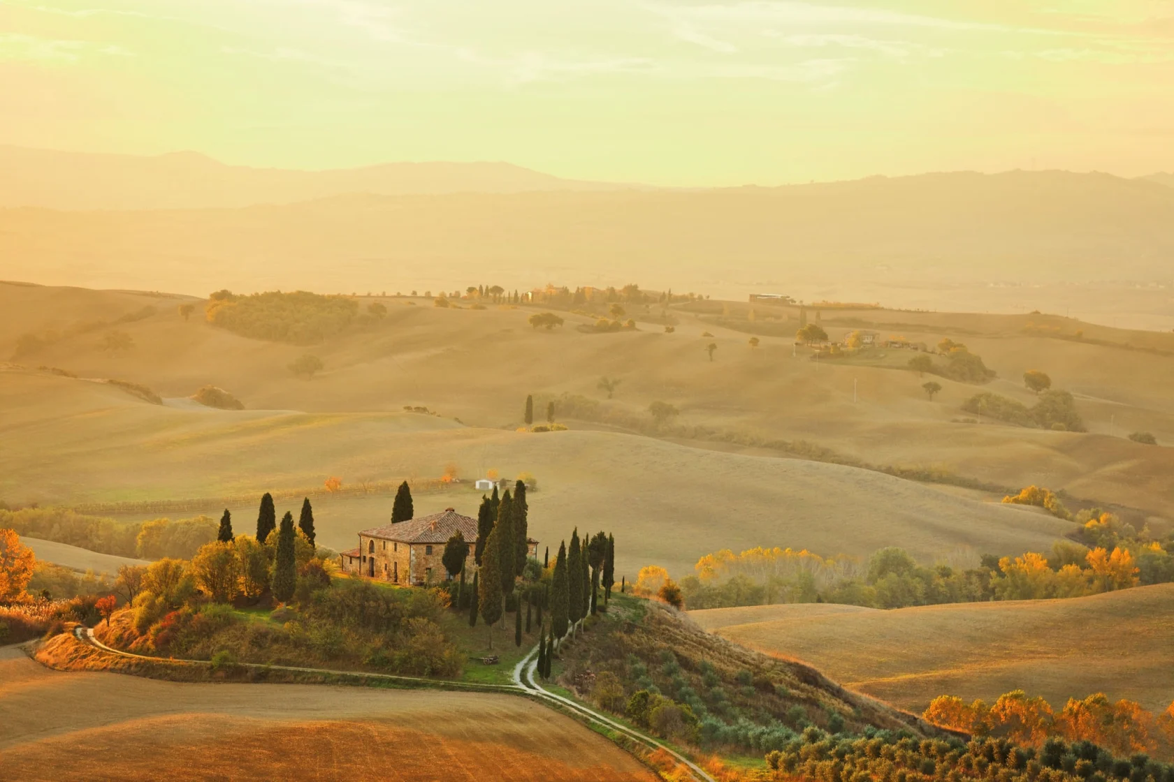 A picturesque landscape of rolling hills at sunset, with a stone house surrounded by trees and winding paths in the foreground.