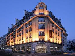 A grand multi-story building with ornate facade lighting stands against a twilight sky.