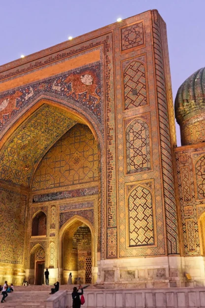 A large, ornately decorated building with a domed roof and intricate patterns, featuring arches and a minaret, against a twilight sky.