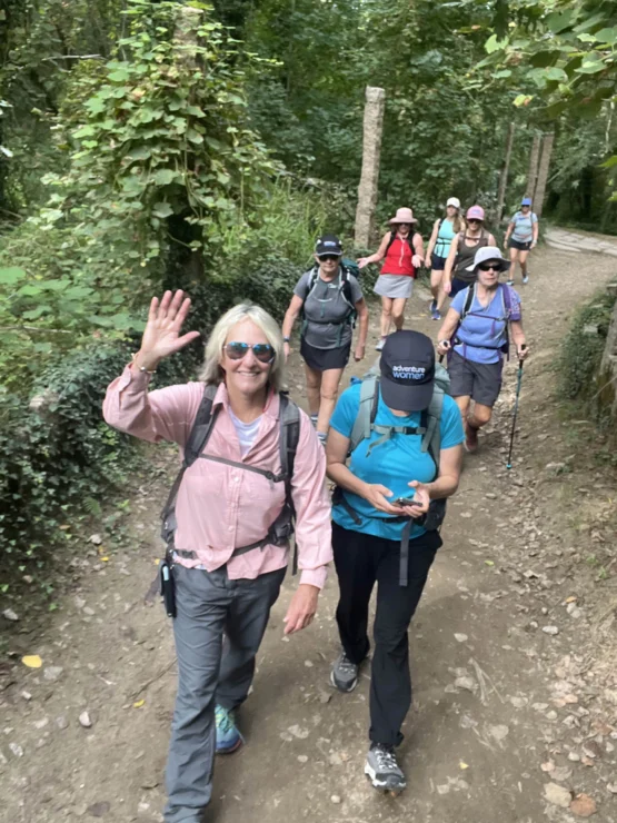 Group of hikers walking on a forest trail. One person in front waves at the camera.