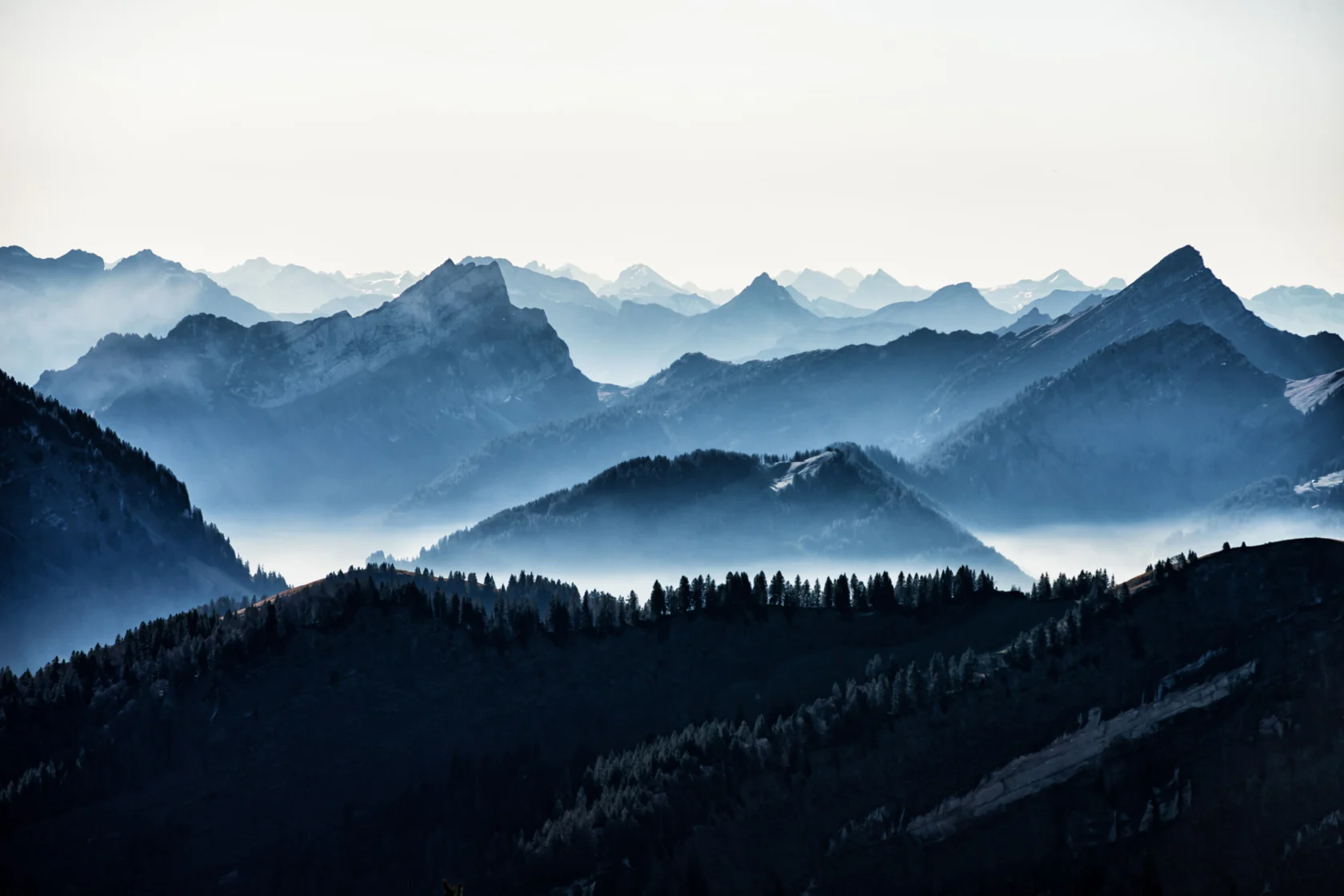 Mountain range with layered peaks and valleys silhouetted against a misty sky at dawn or dusk.