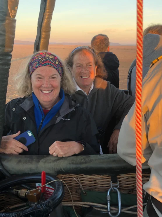 Two people smiling inside a hot air balloon basket, with a desert landscape in the background.