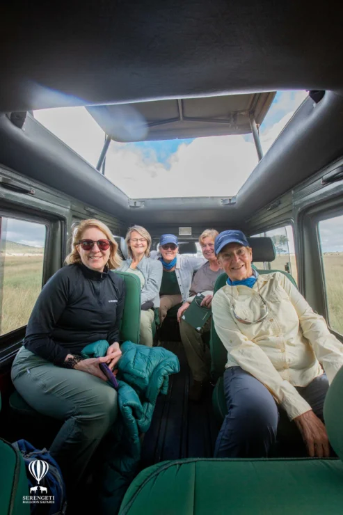 A group of five people in casual outdoor attire sit inside an open-topped vehicle, smiling at the camera.