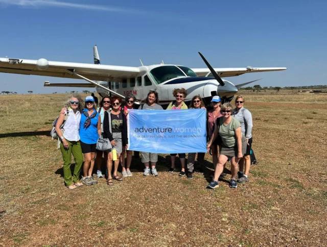 A group of women stand in front of a small airplane holding a banner that reads "adventure women.