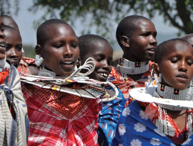 A group of people wearing traditional Maasai clothing and elaborate beaded jewelry, standing outdoors.