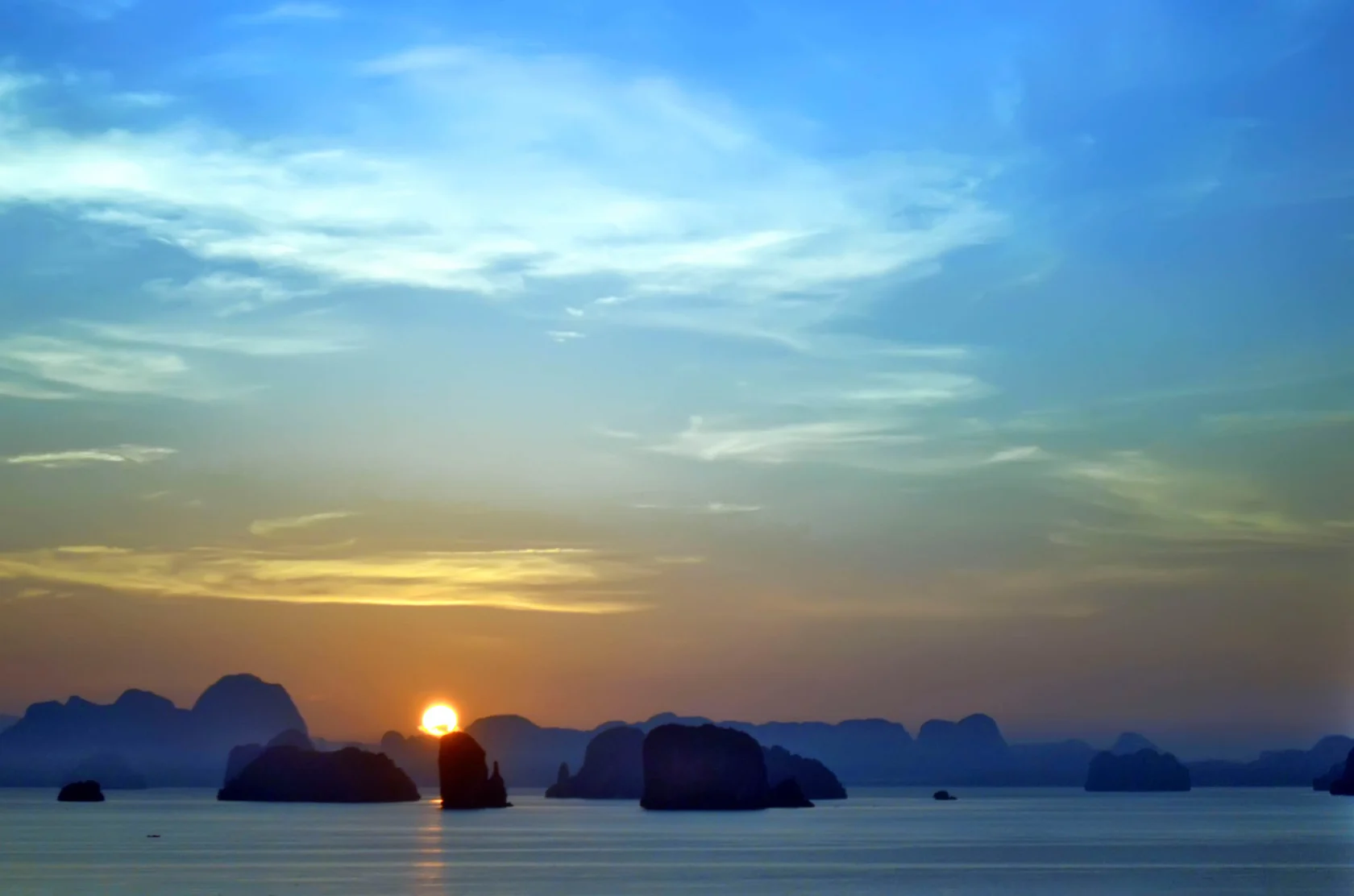 A sunset over the ocean with silhouetted rocky islands beneath a colorful sky.