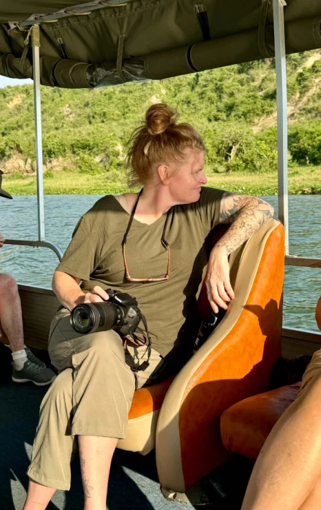 Person with a camera sits on a boat, looking toward the water.