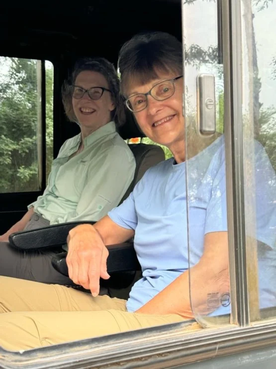 Two people smiling and sitting inside a vehicle, with the window open.