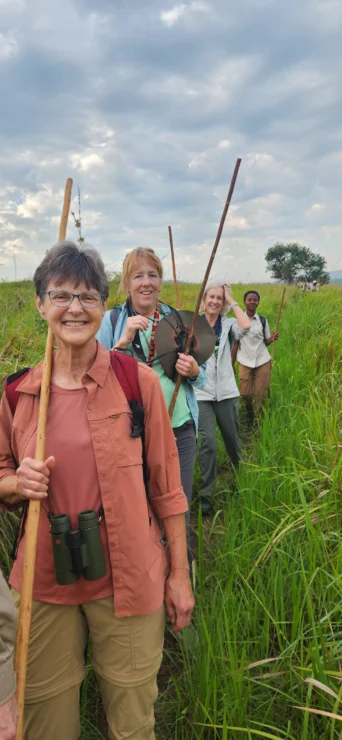 Group of people holding walking sticks in a grassy field under a cloudy sky.