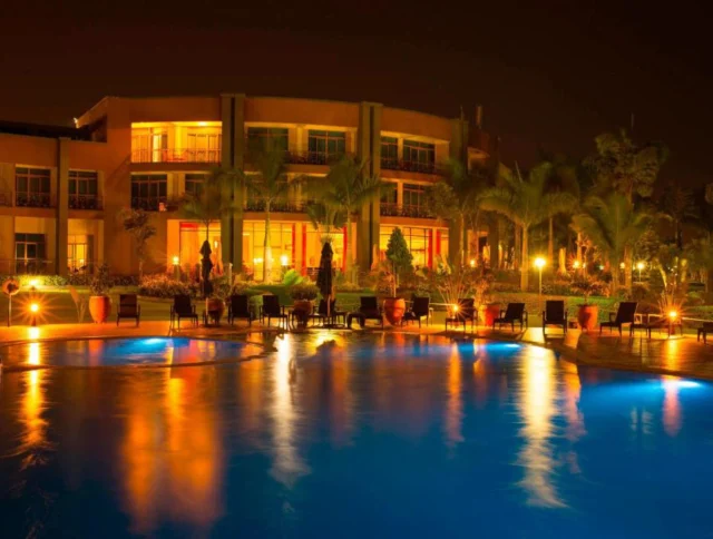 Illuminated building and palm trees reflecting on a tranquil pool at night, with a circular children's pool in the foreground.