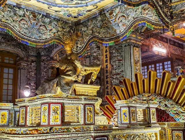 Intricately decorated interior of a Vietnamese temple, featuring a seated golden statue surrounded by colorful, ornate details and patterns.