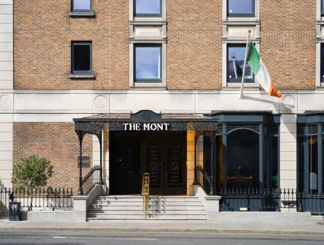 The entrance of The Mont hotel with a glass awning, black doors, and an Irish flag mounted on the building’s facade.