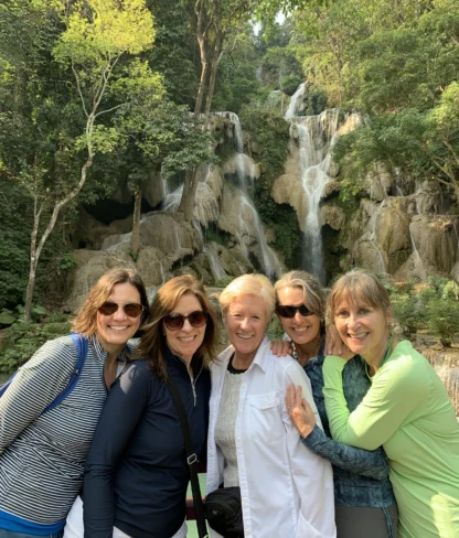 Five people standing together smiling in front of a lush waterfall surrounded by greenery.