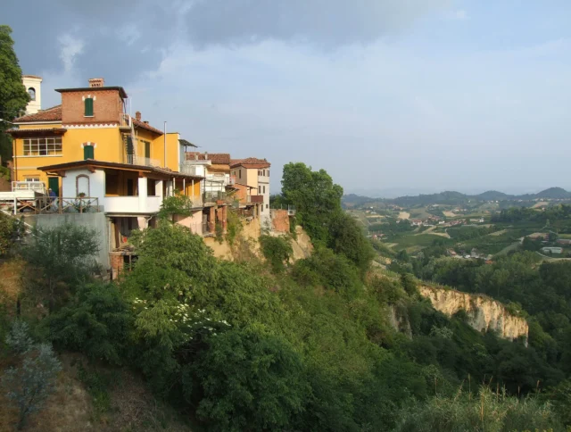 Colorful houses on a hillside overlook a lush green valley under a cloudy sky.