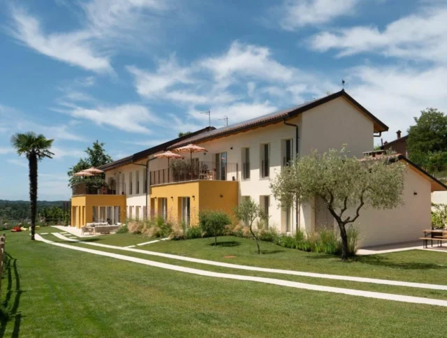 A modern two-story house with a yellow and white exterior, set in a landscaped yard with a palm tree and a walking path under a blue sky with scattered clouds.