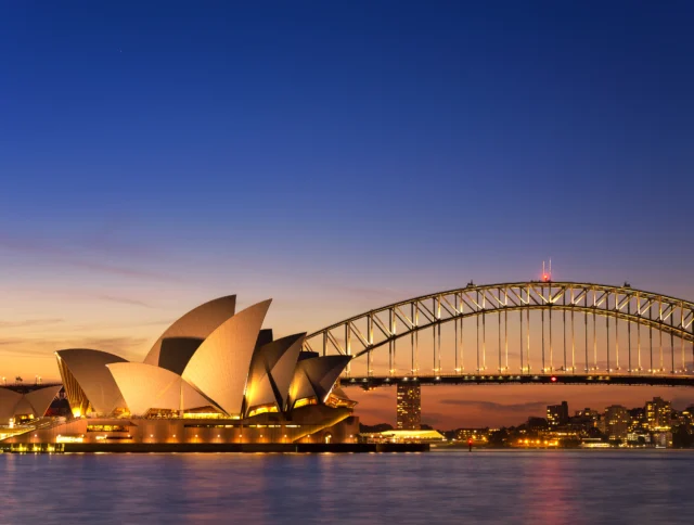 Sydney Opera House and Harbour Bridge at dusk, with illuminated sails and cityscape in the background.