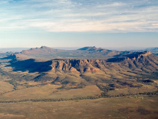 Aerial view of the Flinders Ranges with rugged mountain peaks and expansive valleys under a partly cloudy sky.