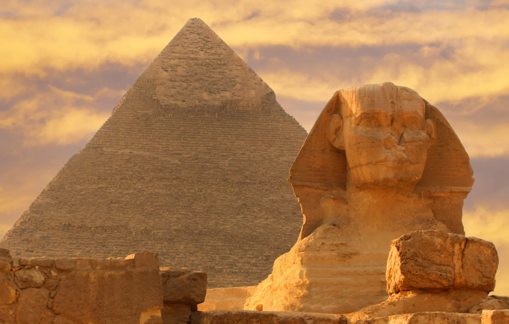 The image shows the Great Sphinx and a pyramid in Giza, Egypt, under a cloudy, golden sky.