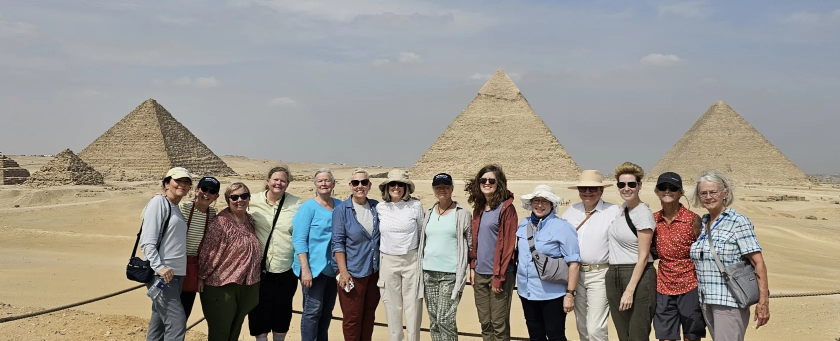 A group of people stand in front of the pyramids in a desert setting.