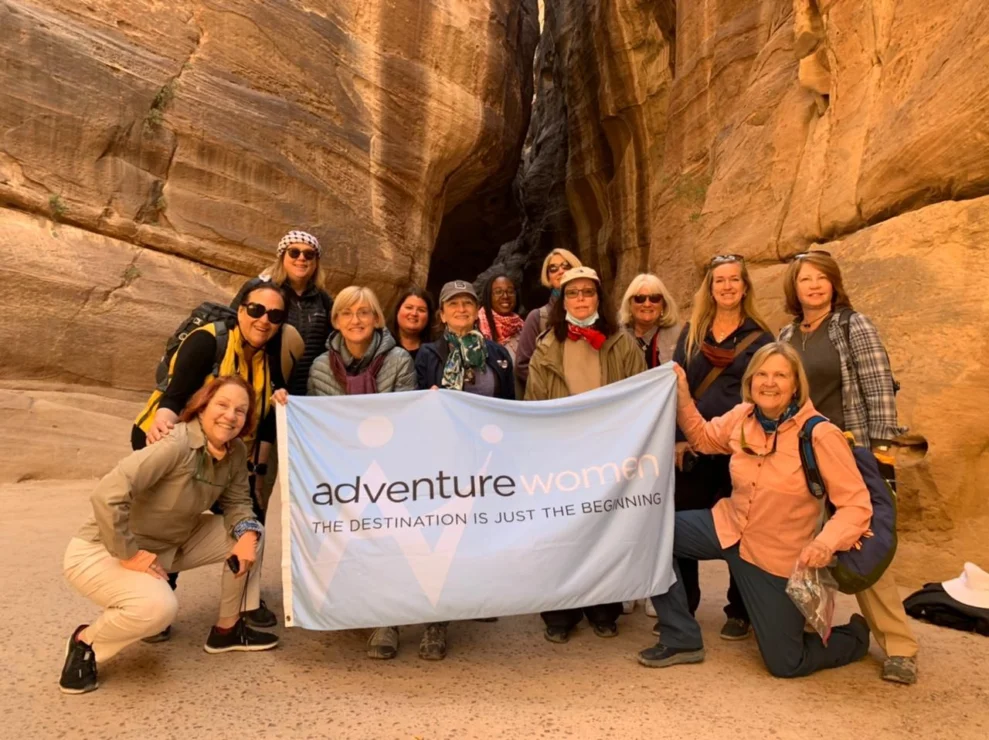 A group of women poses with an "Adventure Women" banner in front of a sandstone rock formation.