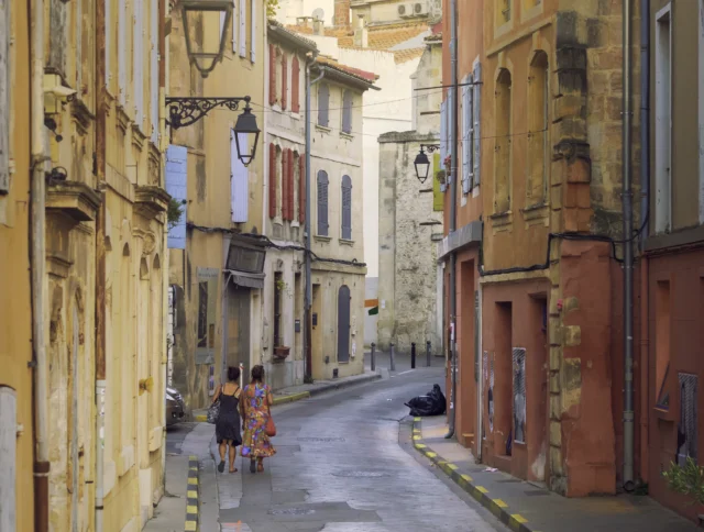 Two people walk down a narrow, empty street lined with colorful, old buildings.