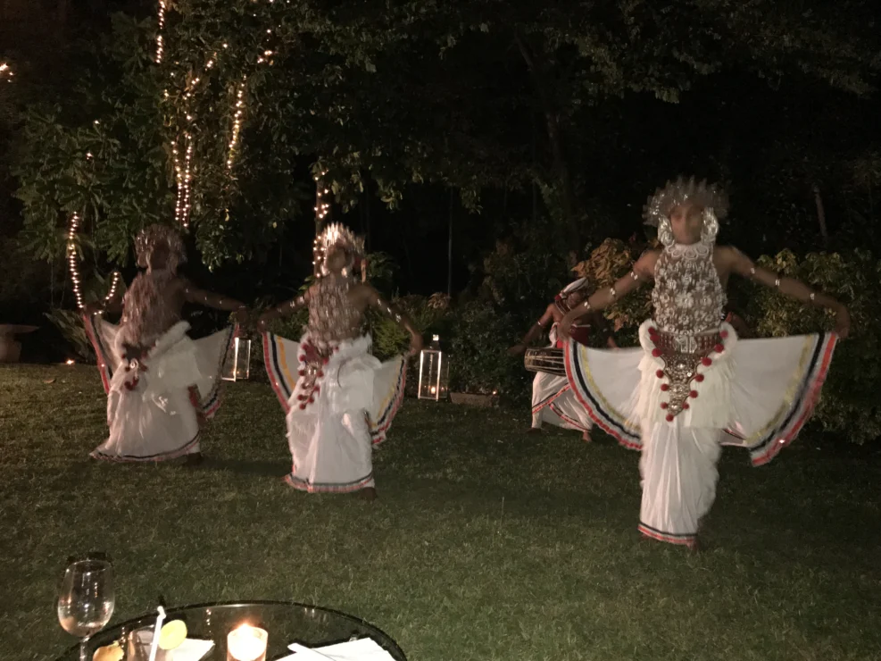 Four dancers in traditional attire perform outdoors at night, illuminated by decorative lights.