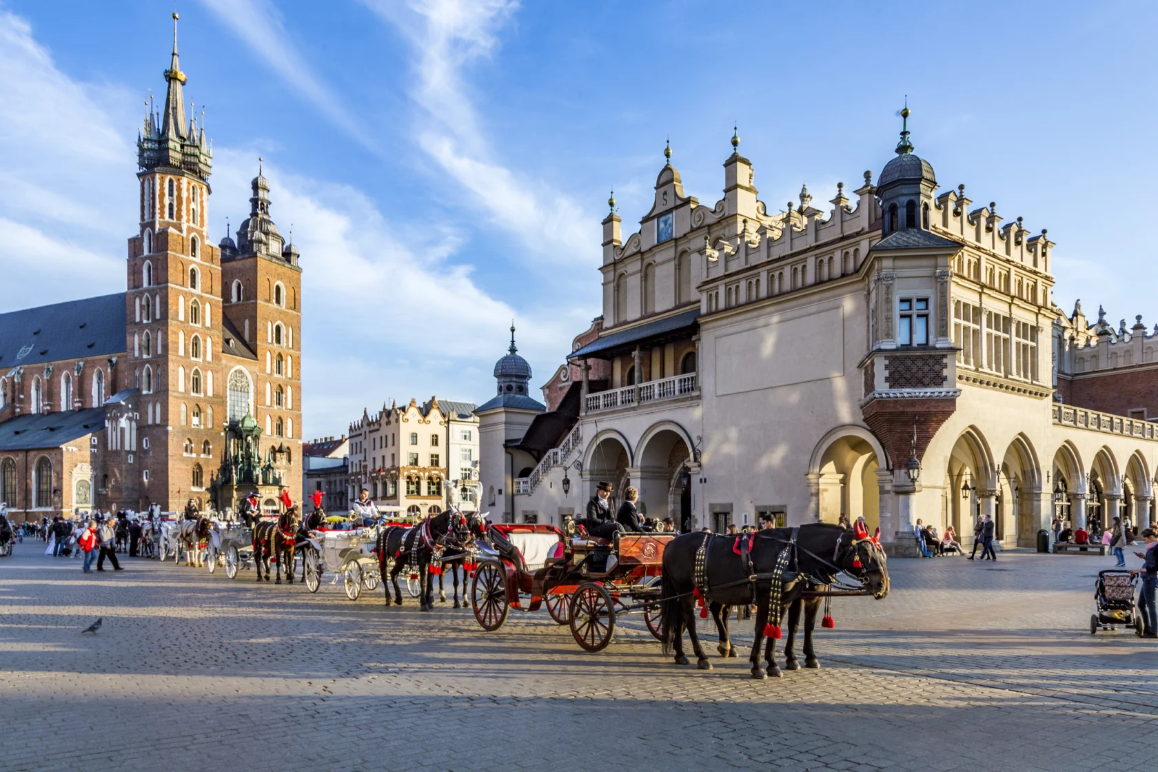 Horse-drawn carriages line a cobblestone square in front of historical buildings under a clear blue sky.