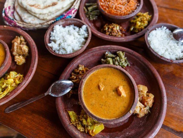 A meal with plates of curry, rice, vegetables, and chutney on a wooden table.