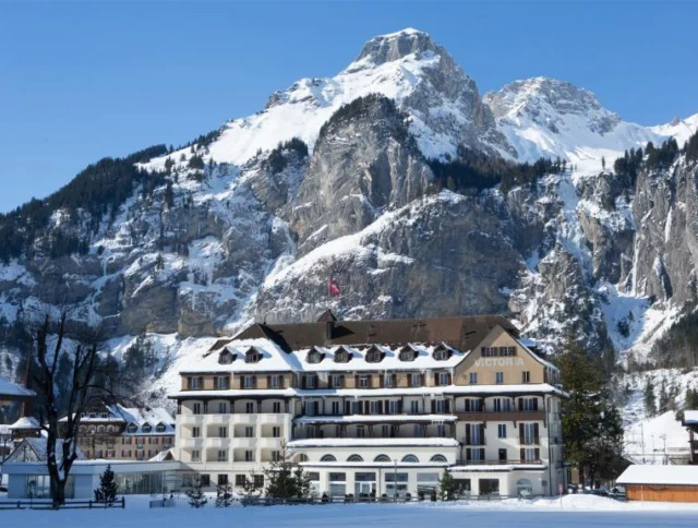 Large hotel named Victoria in front of snow-covered mountains, with a clear blue sky.