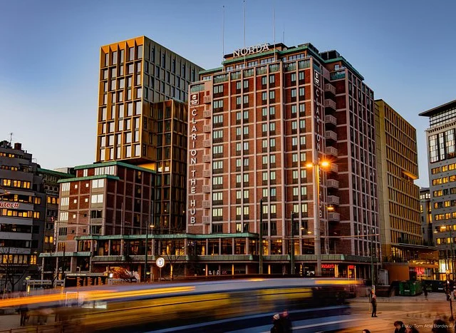 An urban scene at dusk features a large hotel building named "Clarion the Hub" with a blend of modern and classic architecture. A street with blurred motion from vehicles is in the foreground.