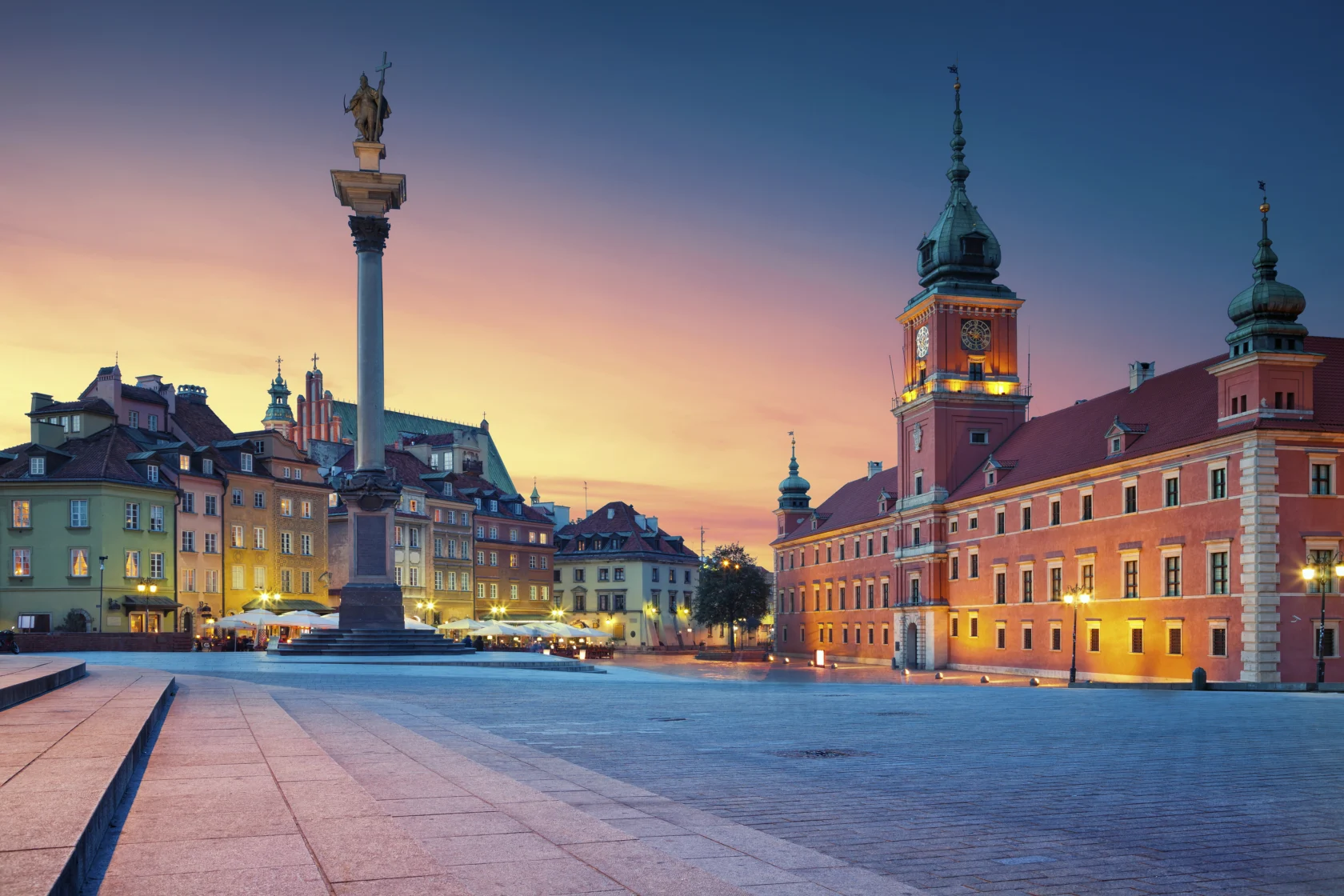 Castle Square in Warsaw at sunset, featuring the Sigismund's Column and the Royal Castle with illuminated historic buildings.