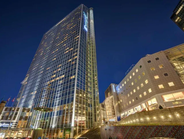 Tall modern glass skyscraper and adjacent buildings illuminated at night, with steps leading up in the foreground.