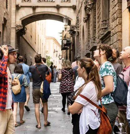 A tour guide talks to a group of tourists on a narrow, historic street with stone buildings and an arched bridge overhead.