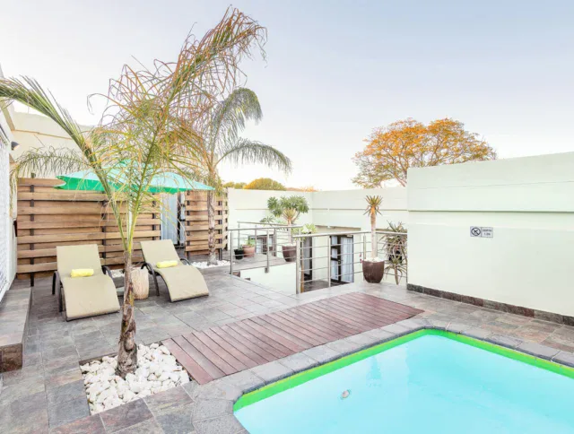 Outdoor patio area with two lounge chairs, a small pool, potted plants, and a wooden deck, surrounded by a white privacy wall.