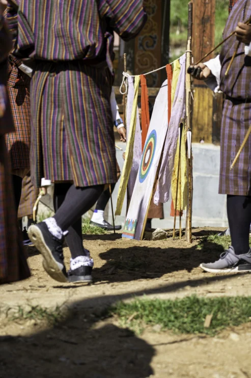 A group of people in traditional striped clothing stand near archery target flags outdoors on a sunny day.