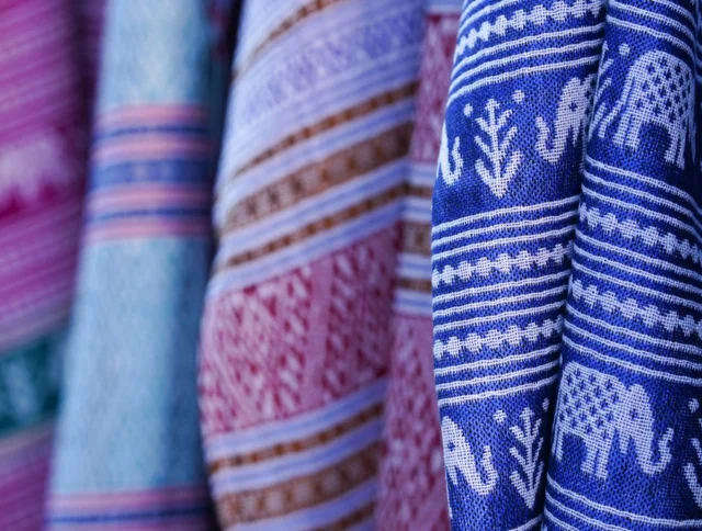 Colorful woven fabrics featuring intricate patterns and designs, including elephants and geometric shapes, hanging closely together.